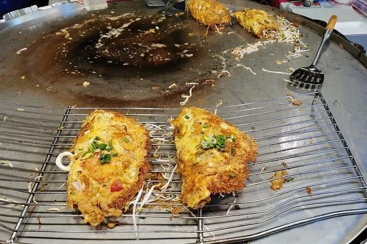 Two large omelets cooking on a large flat metal grill at a market.